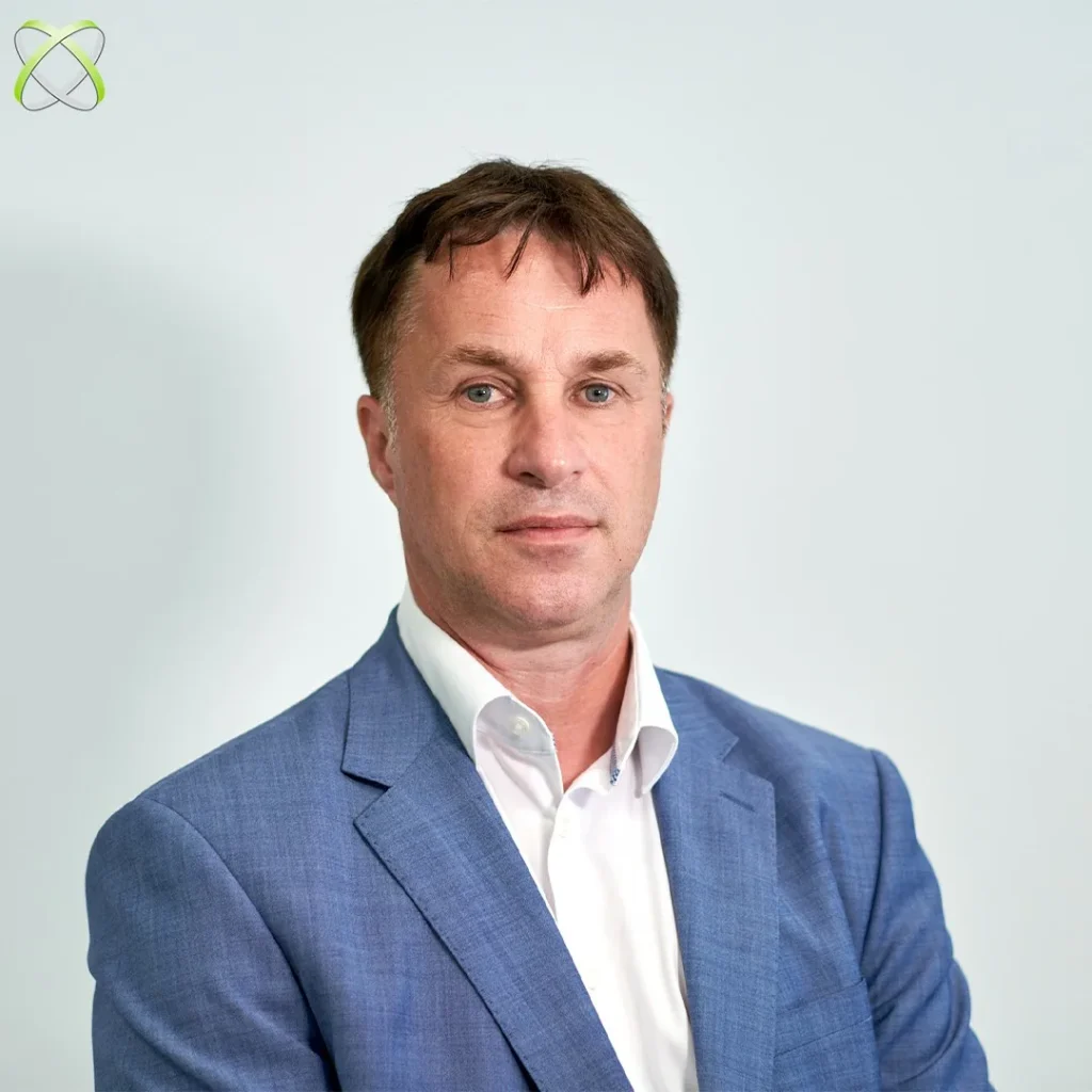 Muškarac u svijetloplavom sakou i bijeloj košulji pozira na običnoj svijetloj pozadini. U gornjem lijevom kutu pojavljuje se zeleni i sivi logotip.