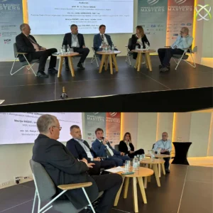 Šest ljudi u poslovnoj odjeći sjedi na pozornici u panel raspravi, s velikim projiciranim platnom iza njih koje prikazuje detalje događaja. Mali stolovi s bocama vode postavljeni su ispred svakog sudionika.